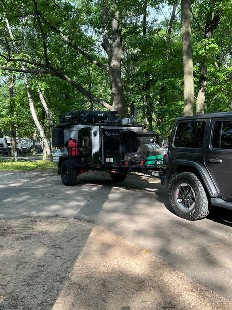 Rugged gray Jeep pulls a black 'Houtla Rentals' overland camper trailer, an ideal RV rental for outdoor trips.
