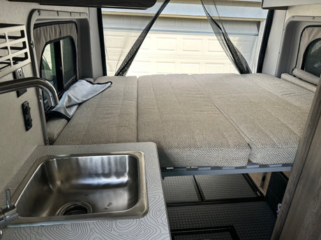 Explore a comfortable RV rental! Features a spacious bed, functional kitchen sink, and clever storage solutions.