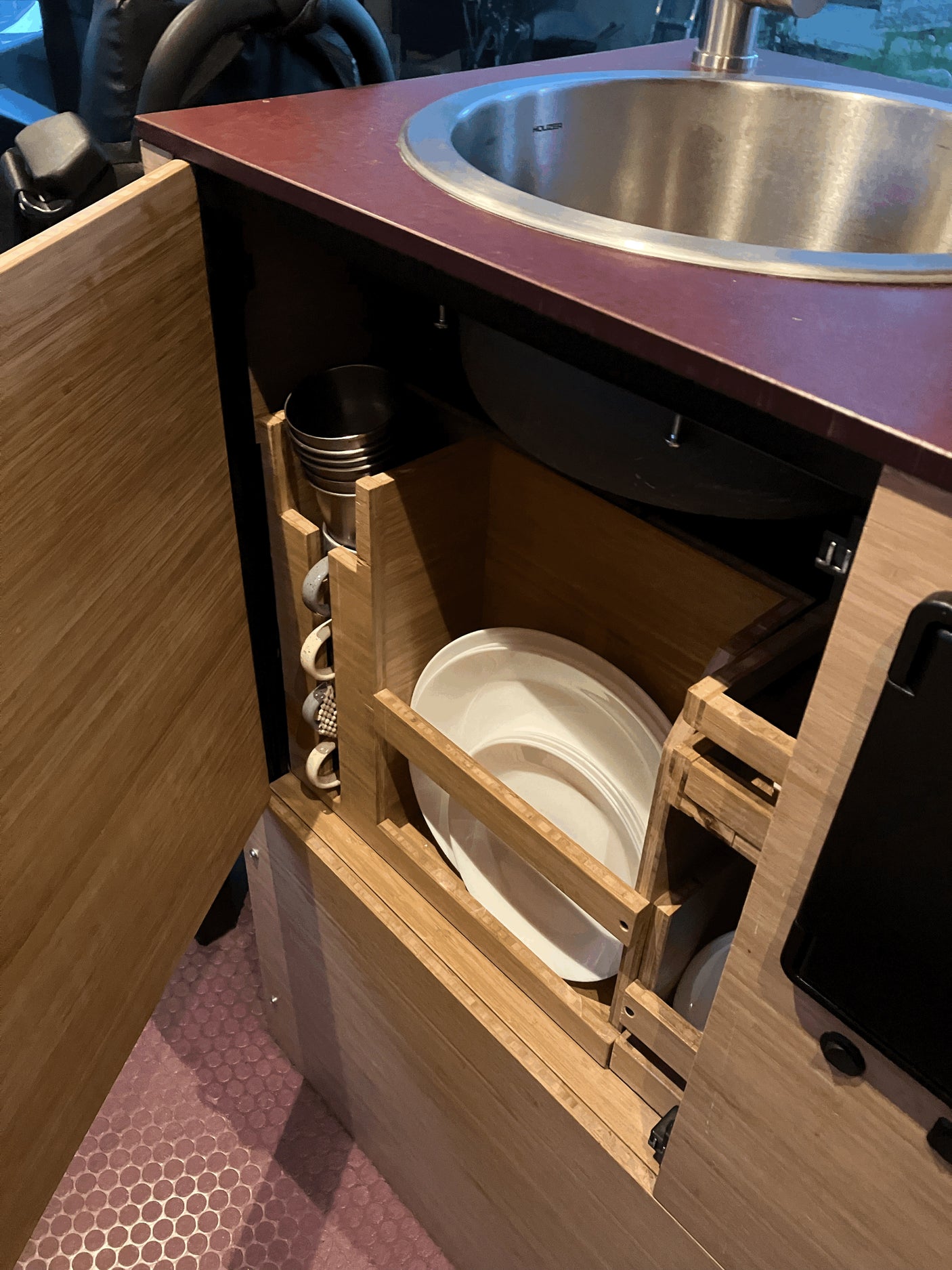 RV rental kitchenette with compact sink, custom wood storage for plates, cups, and a pan, designed for travel.