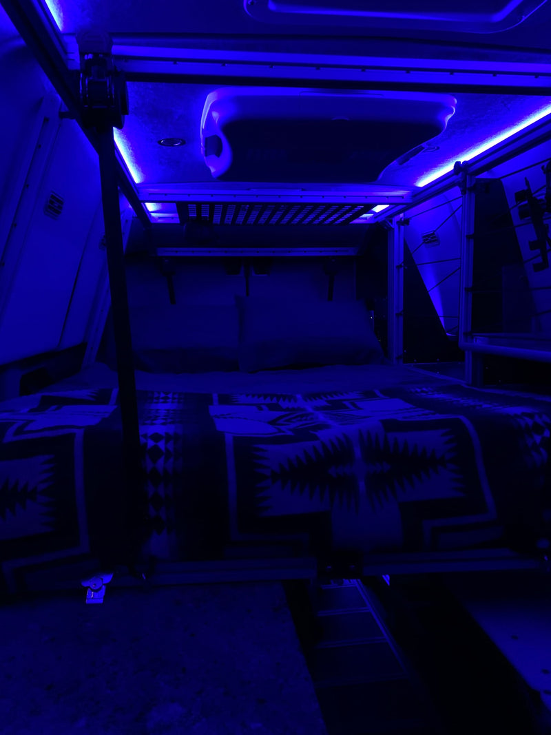 Modern RV rental interior, showcasing a bunk bed or sleeping pod with ambient blue LED lighting and a patterned blanket. — photo 12