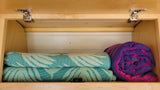 RV rental storage: Light wood cabinet with rolled colorful blankets, door hinges, and a magnetic latch.