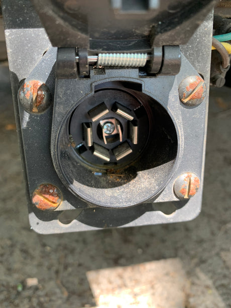 Close-up of a rusty 7-pin trailer connector on a vehicle, essential for rv rental towing.