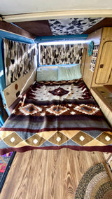 Cozy RV rental interior showing a bed with a patterned blanket, wood floors, and inviting camper van decor.