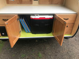 Organized RV rental galley setup with a large Igloo cooler, folded mats, and wood cabinetry for compact storage.