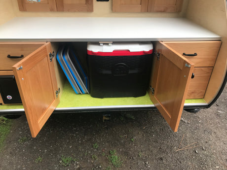 Organized RV rental galley setup with a large Igloo cooler, folded mats, and wood cabinetry for compact storage.