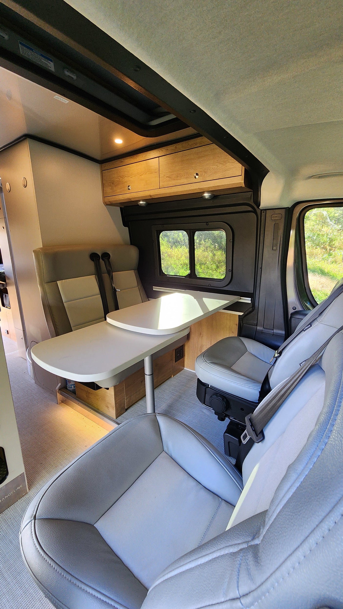 Spacious rv rental interior featuring a dining table with two rear seats, two swiveling front seats, and large windows.