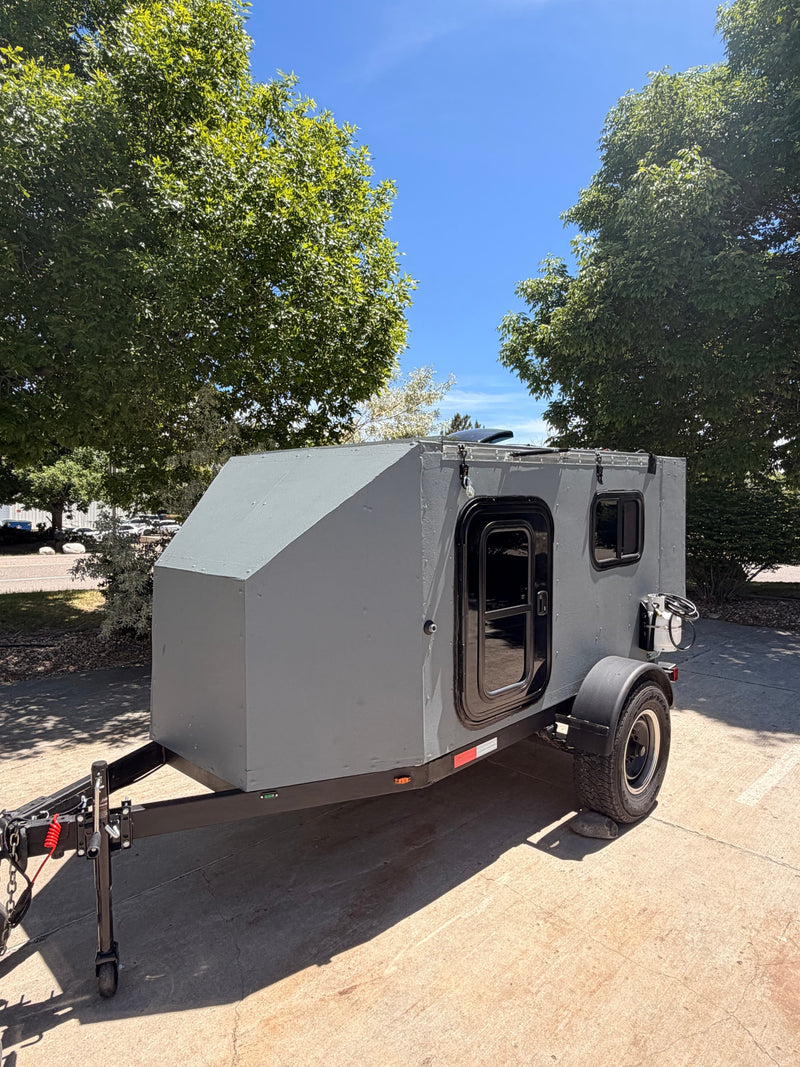 Compact gray camper trailer, ideal for an rv rental. Features a door, window, roof vent, and side-mounted propane tank. — photo 6
