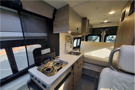 Clean RV rental interior: compact kitchen with stove & sink, plus cozy seating/bed area, perfect for travel.