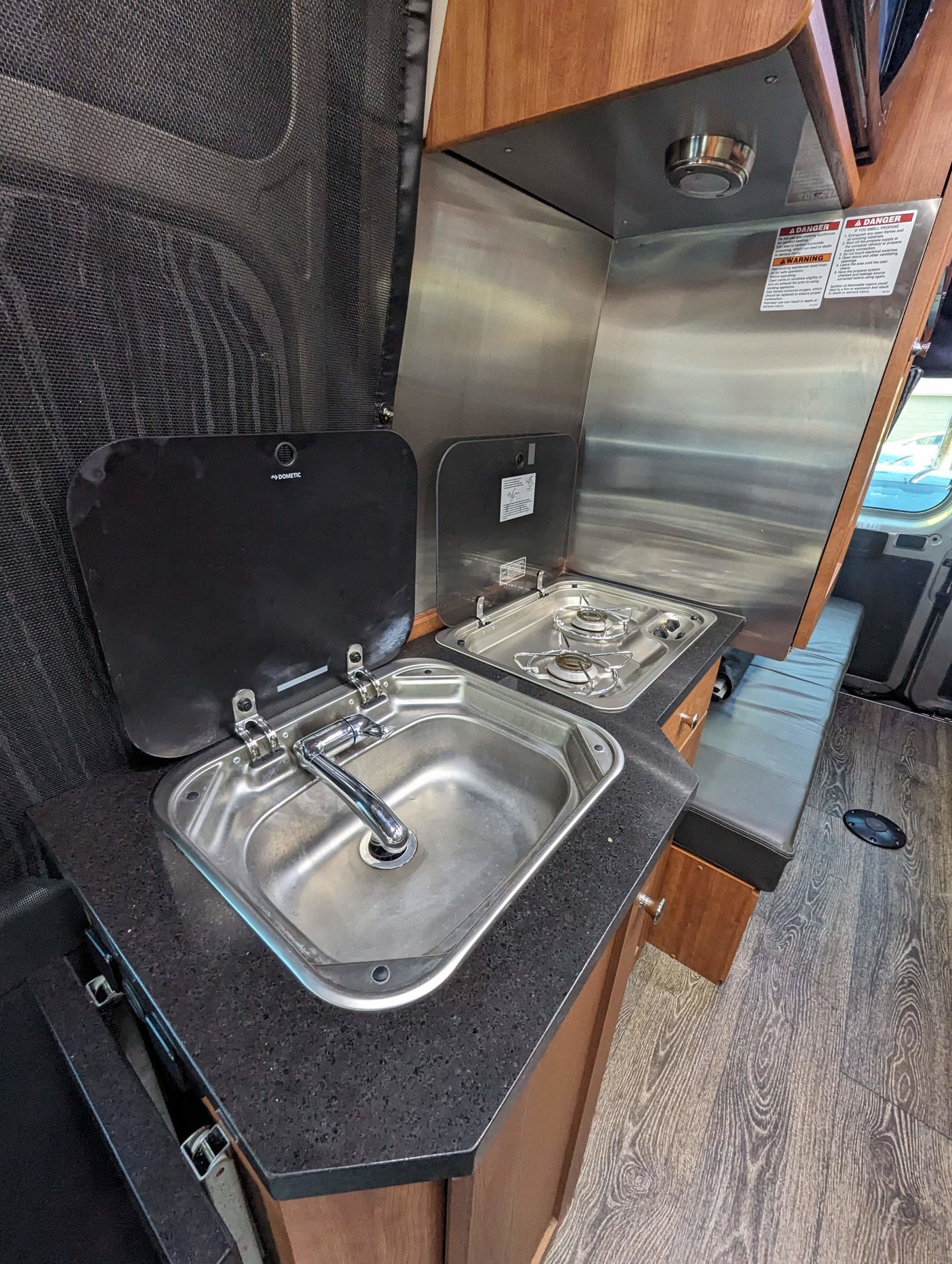 An RV rental kitchen showcasing a stainless steel sink, two-burner stove, and dark countertop for cooking on the go.