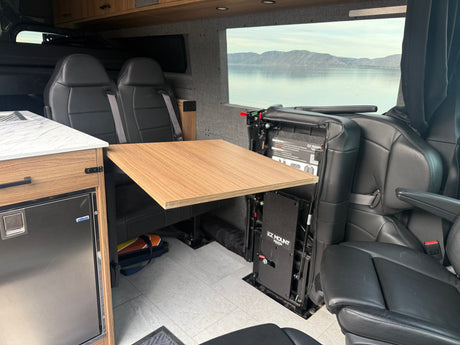 This RV rental interior features comfortable seating, a versatile table, an Isotherm fridge, and a stunning lake view.