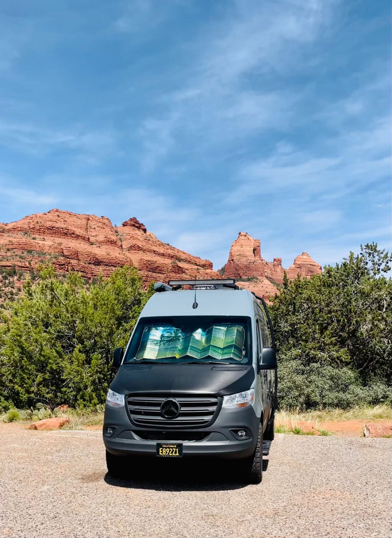  parked on gravel with stunning red rock mountains and green shrubs in the background. Perfect for adventure.|Explore with this RV rental! Rear view of a custom camper van with open doors — photo 12