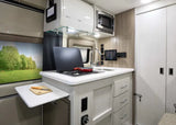 RV rental's compact kitchen: cooktop, sink, microwave, pull-out counter, and window view of nature.