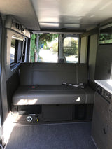 RV rental interior: a comfy gray bench seat, kitchenette, and accessible controls, ideal for your next adventure.