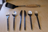 RV rental ready: Camping spatula & full stainless steel cutlery set (2 forks, 2 spoons, 2 knives) on a light wood surface.