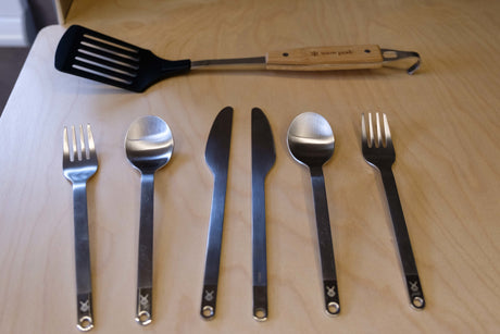 RV rental ready: Camping spatula & full stainless steel cutlery set (2 forks, 2 spoons, 2 knives) on a light wood surface.