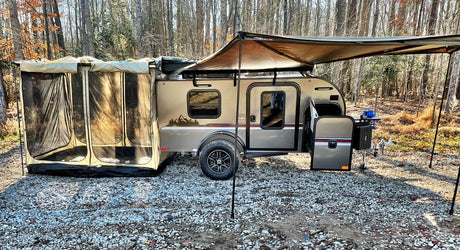 Modern teardrop RV rental camper with screen room & awning at a gravel campsite, ready for adventure.