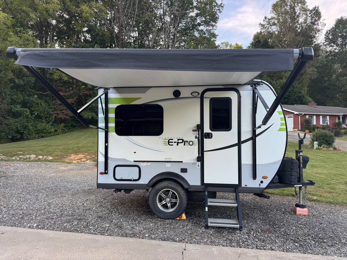  sits parked on a gravel driveway near a house.|This white and green Flagstaff E-Pro travel trailer — photo 3