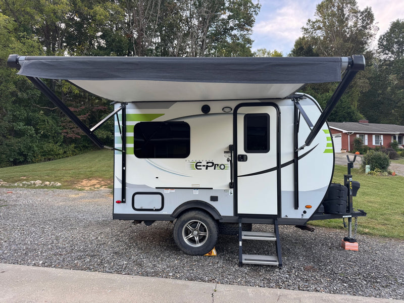  sits parked on a gravel driveway near a house.|This white and green Flagstaff E-Pro travel trailer — photo 3