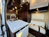 RV rental interior: featuring dark wood cabinetry, a functional kitchen with sink, and a cream bench seat for comfortable travel.
