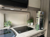 Clean RV rental kitchen: countertop, sink, Dometic cooktop, Insignia TV, and large water filter for travel.