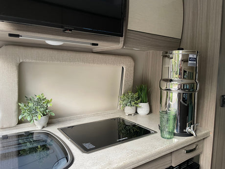 Clean RV rental kitchen: countertop, sink, Dometic cooktop, Insignia TV, and large water filter for travel.