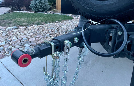 RV rental ready: A trailer hitch receiver with red bushing, attached safety chains, and partial spare tire for towing.