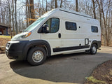 White Winnebago Solis camper van, perfect for an rv rental, parked on an asphalt drive in a sunny, wooded setting.