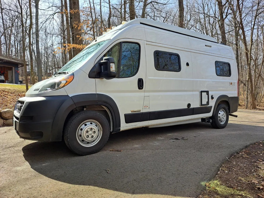 White Winnebago Solis camper van, perfect for an rv rental, parked on an asphalt drive in a sunny, wooded setting.