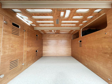 Inside a custom RV rental: wood-paneled interior, built-in storage, patterned ceiling with light strips, and a bright floor.