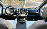 Spacious RV rental interior featuring the dashboard, steering wheel, and front seats, overlooking a forest road.