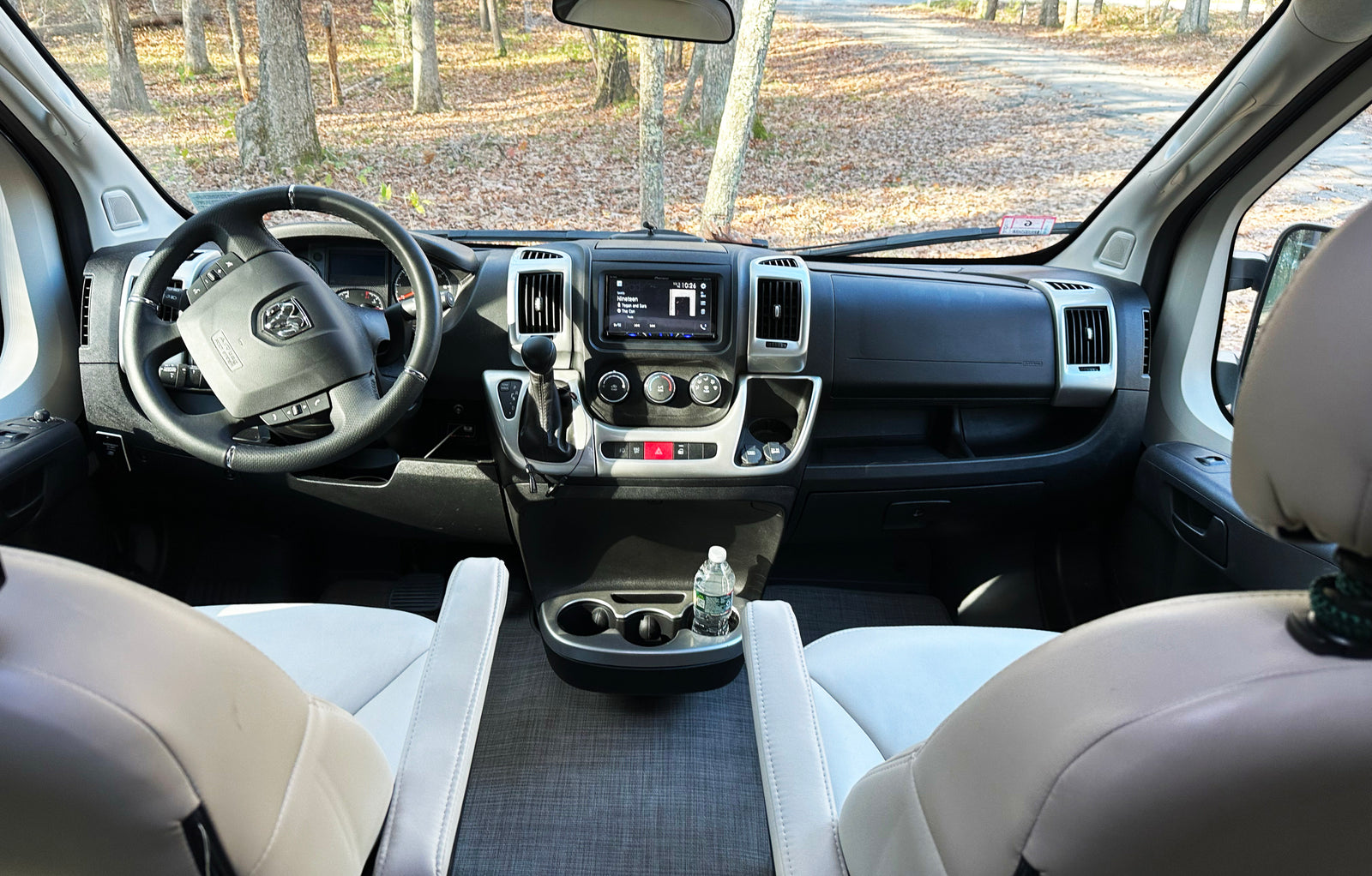 Spacious RV rental interior featuring the dashboard, steering wheel, and front seats, overlooking a forest road.