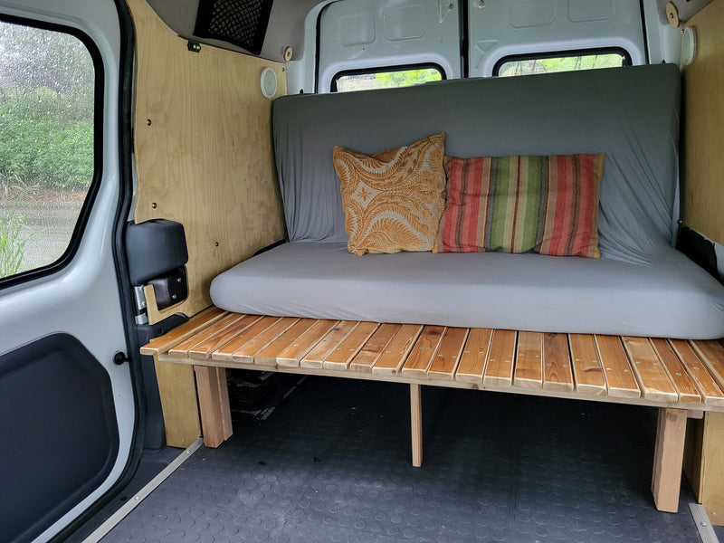  and overhead storage net from the rear seats.|RV rental interior: A comfy bed with colorful pillows in a camper van — photo 7