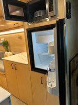 Modern RV rental interior with open microwave, bright refrigerator, and sleek kitchen cabinets.