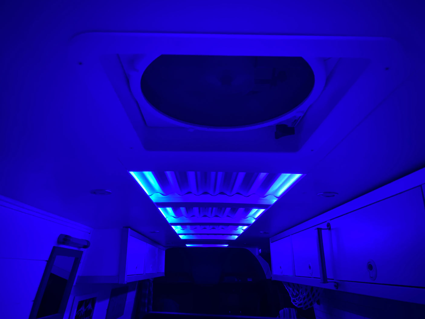 Immerse in the vibrant blue glow of this RV rental's interior. Featuring ambient ceiling lights, a roof vent, and practical overhead storage.