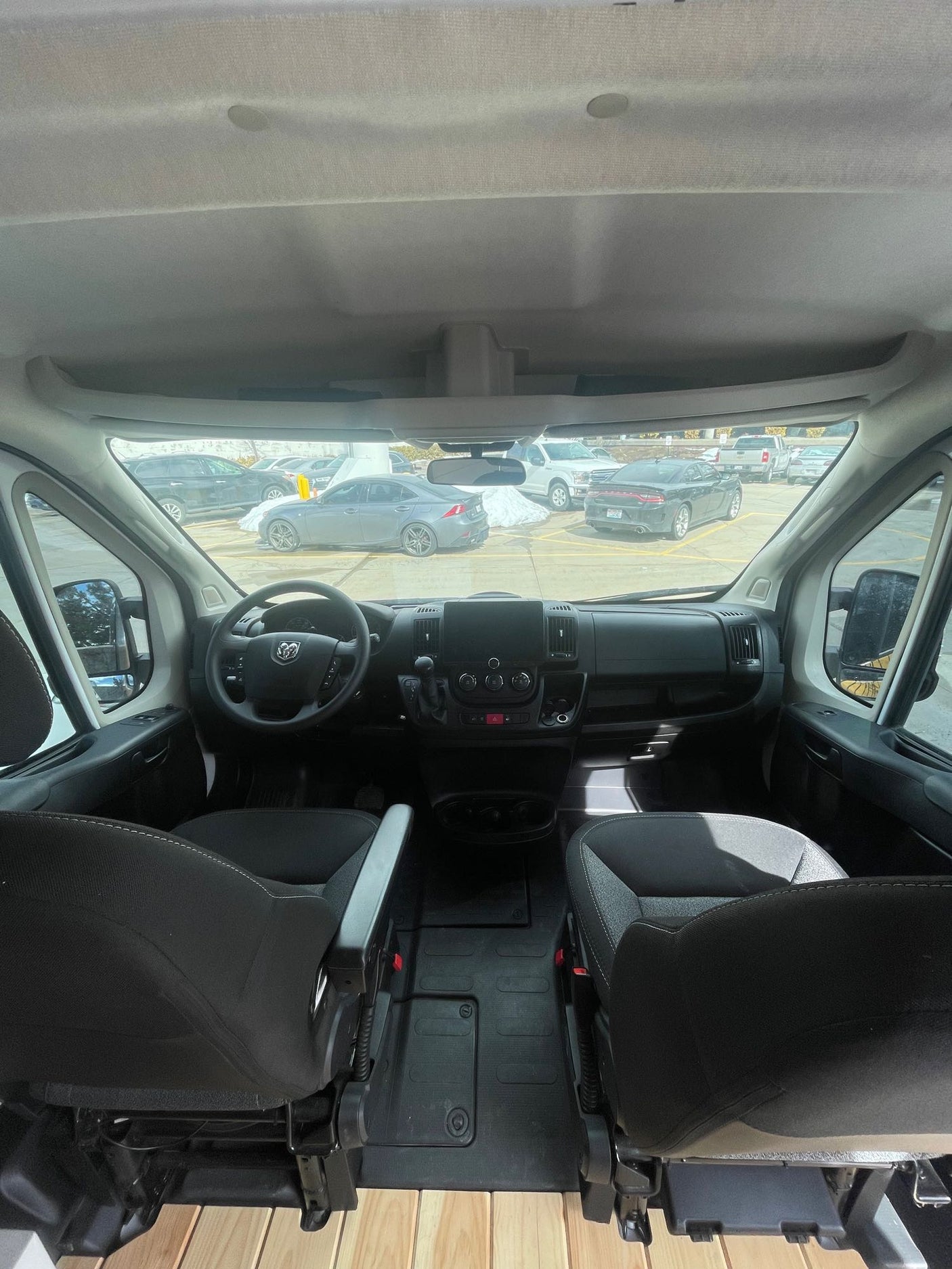 Inside an RV rental: the front cabin shows two seats, a steering wheel, and dashboard. A wooden floor is visible.