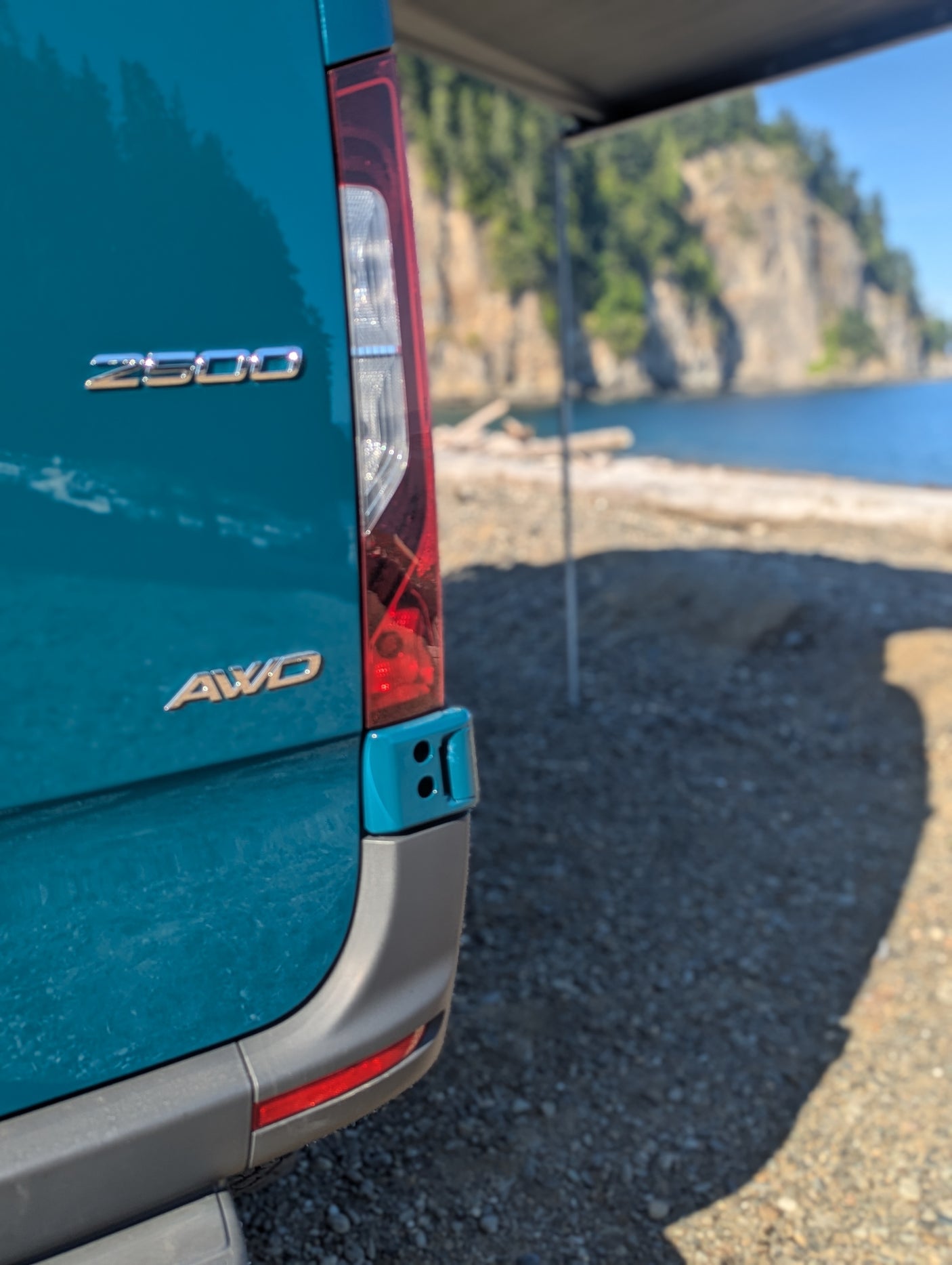 A teal RV rental (2500 AWD) is parked by a stunning coastal cliff and beach, highlighting outdoor adventure capabilities.