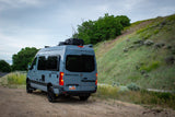 Gray Sanctuary Sprinter RV rental on a dirt road, next to a grassy hill. Explore nature in this converted van.