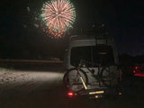Nighttime fireworks illuminate an RV rental with bikes on the rack, a perfect setup for outdoor adventures.