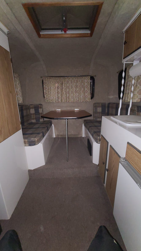 View of an RV rental's compact interior: dinette with plaid benches, table, and small kitchen counter.