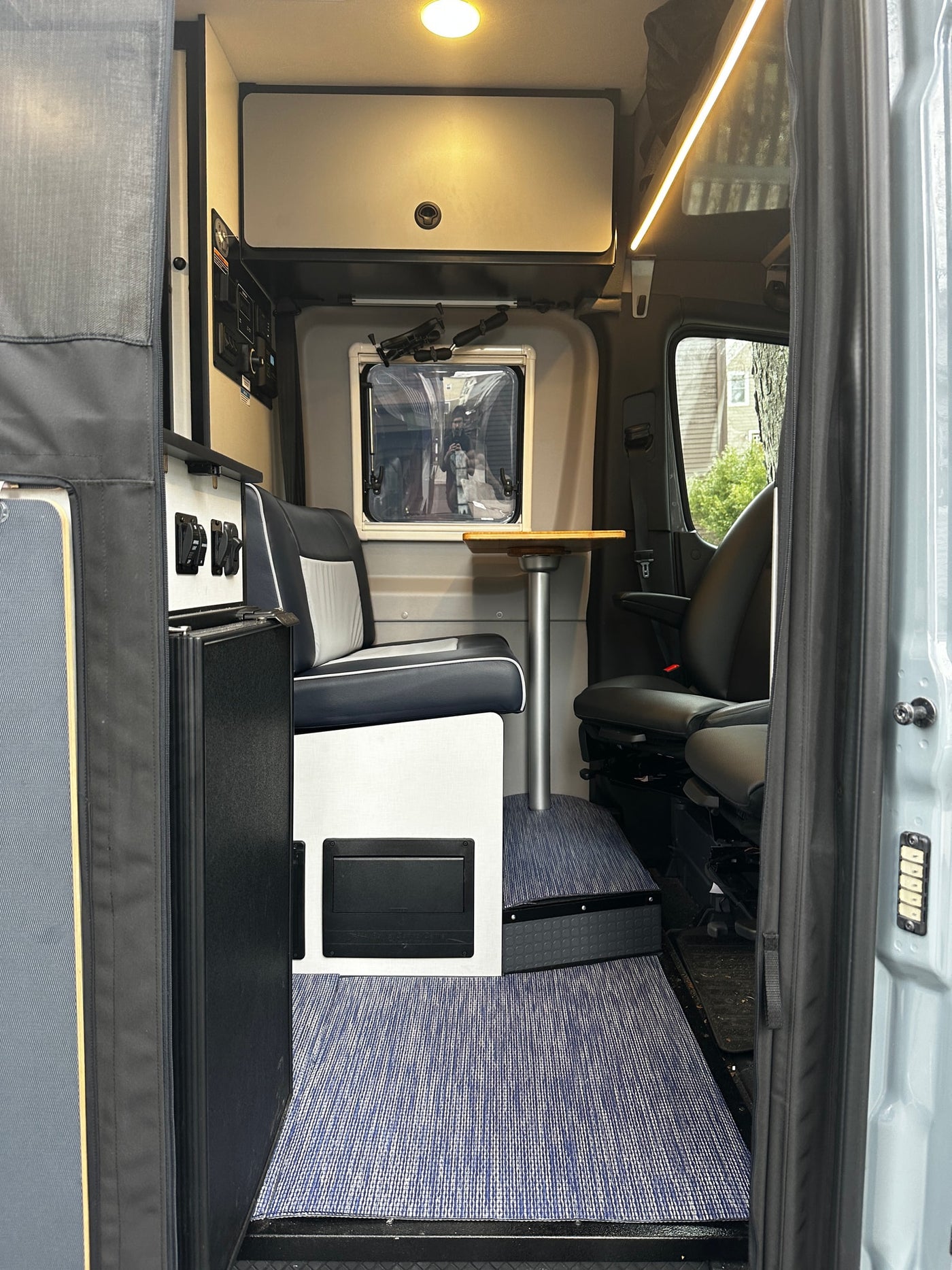 Modern rv rental interior: dinette with table, overhead storage, forward seating, and blue patterned flooring. — photo 13
