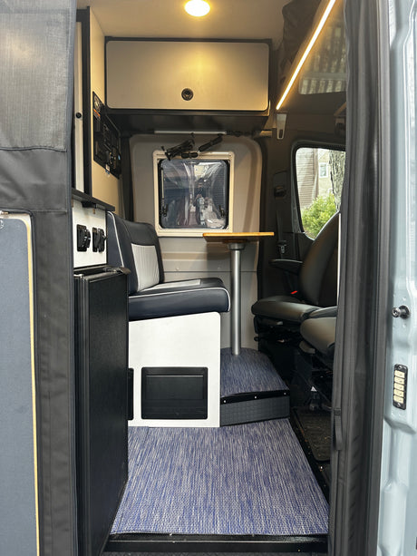Modern rv rental interior: dinette with table, overhead storage, forward seating, and blue patterned flooring.