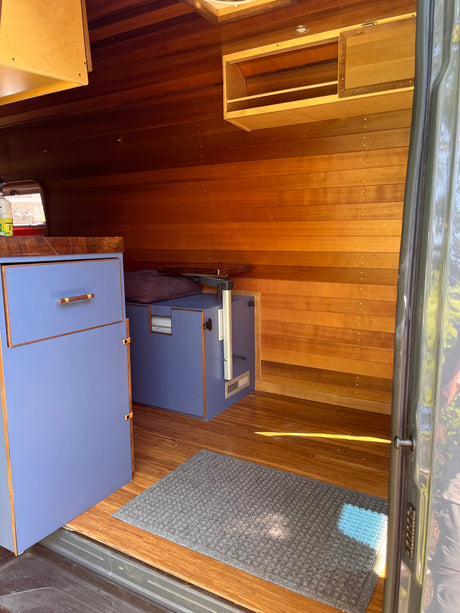 RV rental: Inside a custom camper van with warm wood paneled walls & unique lavender-blue cabinetry.