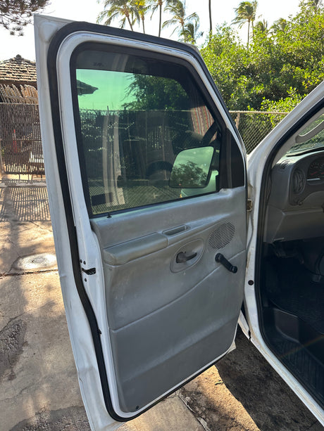 Open driver's side door of an RV rental, showing the interior panel, dashboard, and an outdoor view with palm trees.