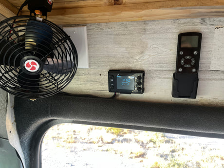 RV rental interior: fan, heater control (P 14.0v), and remote on wood paneling, with a window view below.