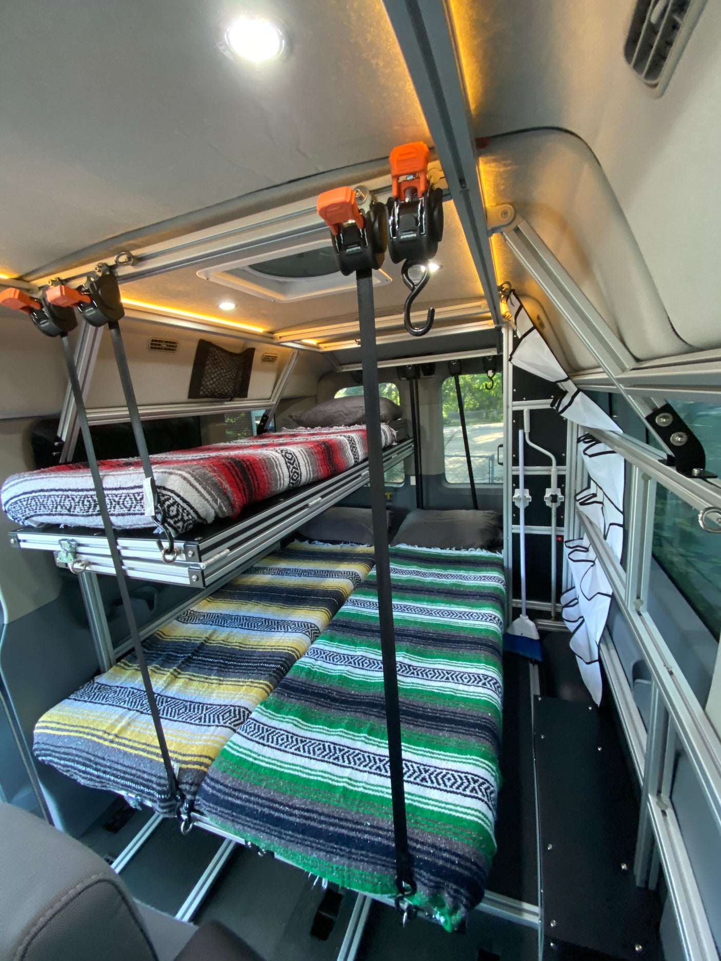 Inside an RV rental: a custom camper van interior with aluminum-framed bunk beds. Two sleeping areas with colorful blankets.