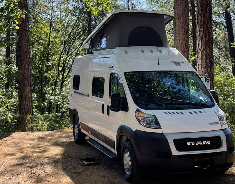  is parked with open doors on a dirt road by the ocean at a golden sunset.|A bright white rv rental campervan is parked at night in a dark forest — photo 2