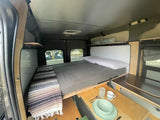 Inside a cozy rv rental camper van: bed with storage above, and a pull-out dining table for compact living.
