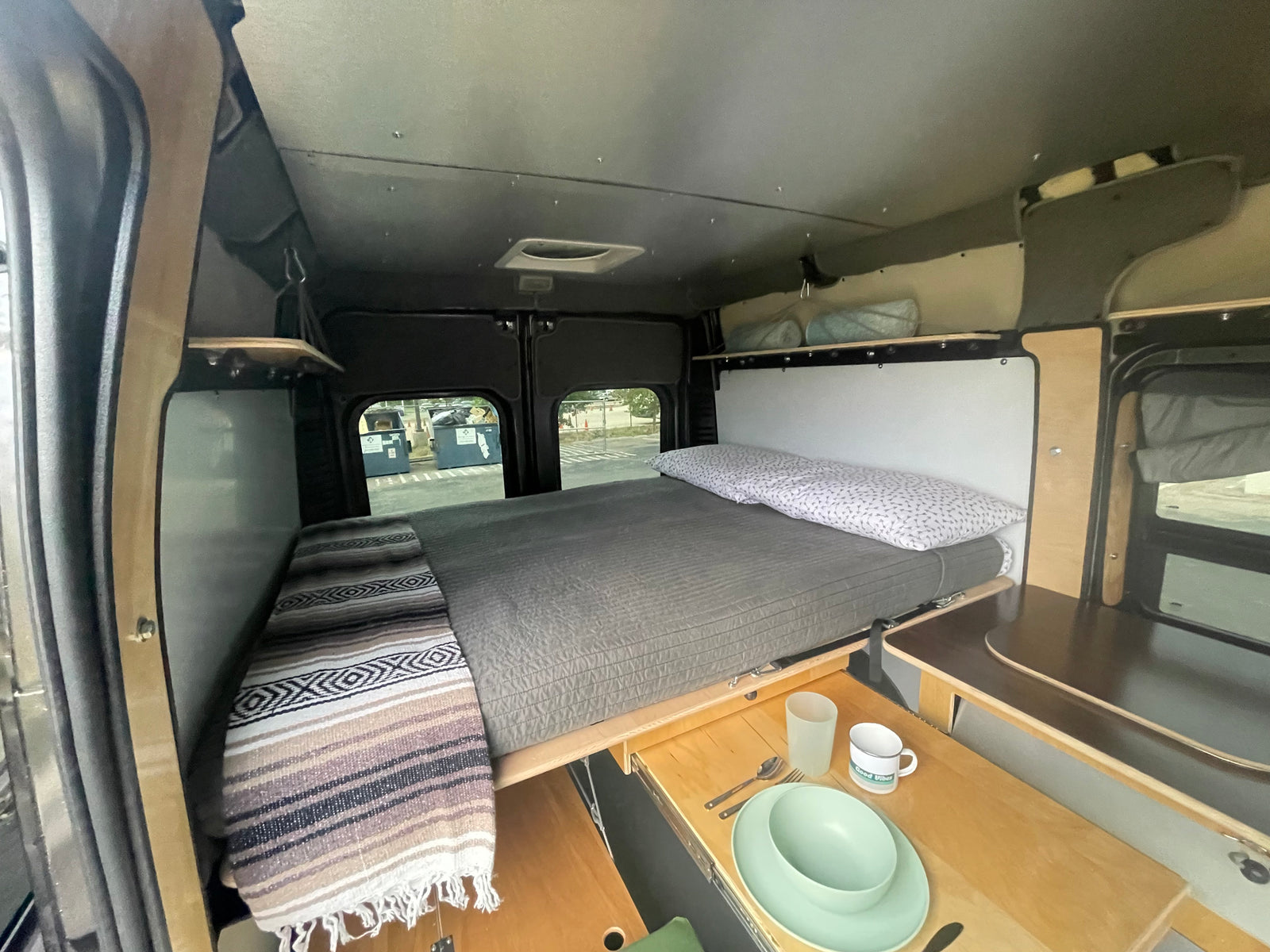 Inside a cozy rv rental camper van: bed with storage above, and a pull-out dining table for compact living.