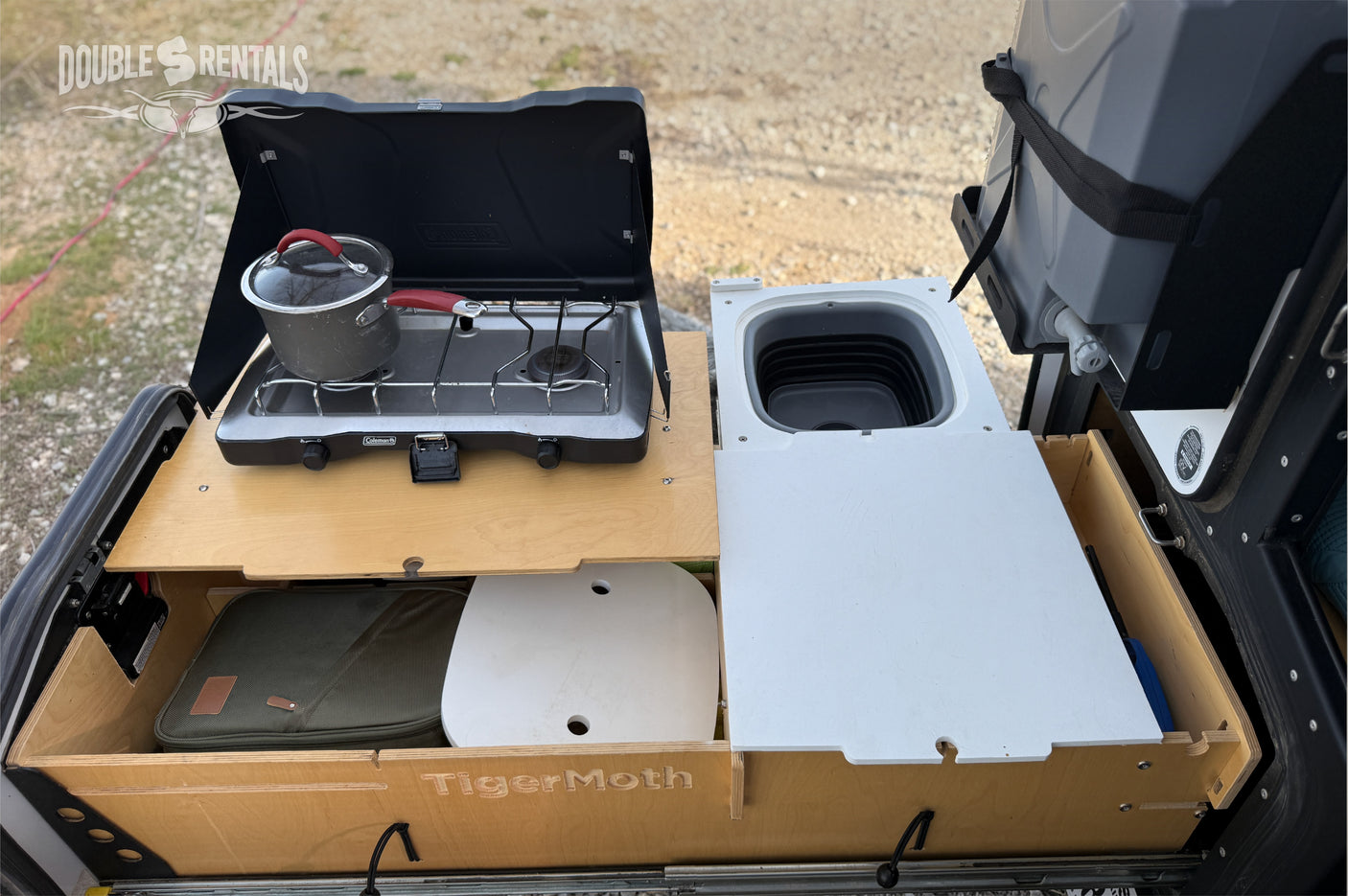 Compact RV rental outdoor kitchen: pull-out stove with pot, collapsible sink, and storage drawers for convenient camping.