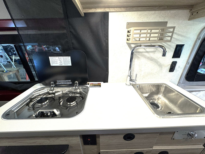 Essential RV rental kitchen setup: a two-burner stove with cover, stainless steel sink, and clean white countertop. — photo 15